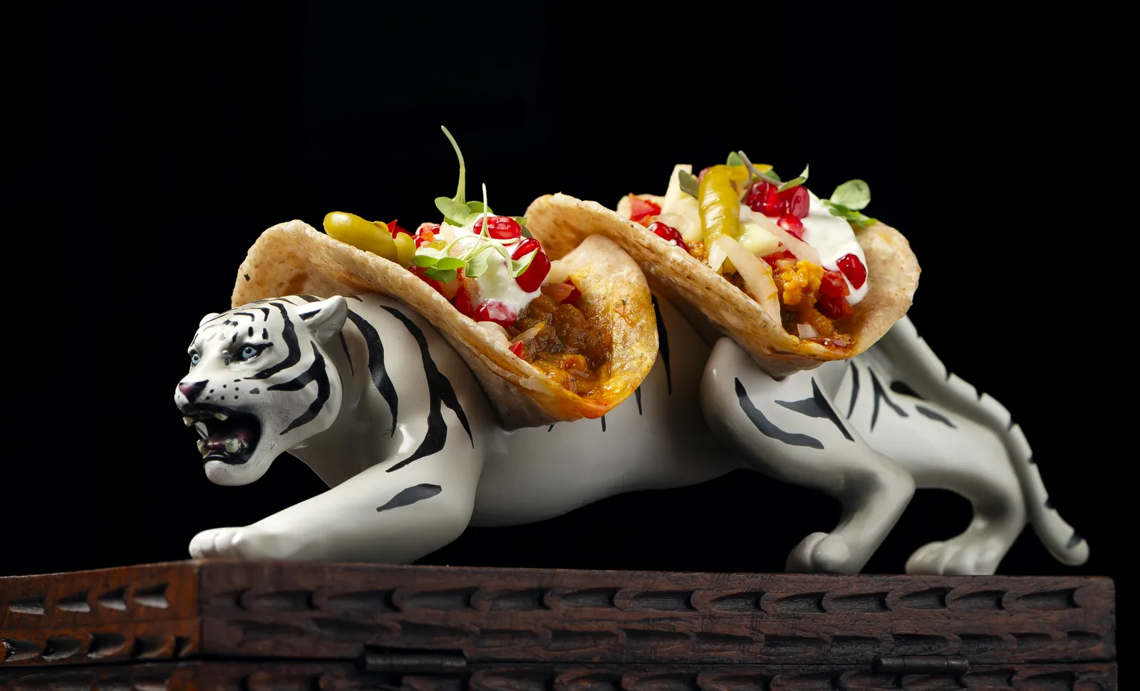 Los Tiger tacos servidos sobre el lomo de un tigre blanco de cerámica: pan paratha con gambas, yogur, granada y guindilla
