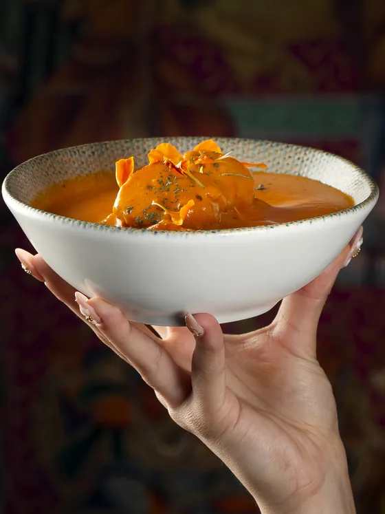 Chicken tikka masala con pétalos de caléndula, en su cuenco sostenido en alto delante de un mural indio